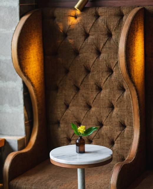 Small round marble table in cafe and bottle with yellow flower. Dark brown background, minimalist modern style